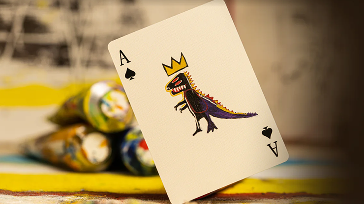 An Ace of spades card featuring a Basquiat painting, placed on a table with various paint tubes.